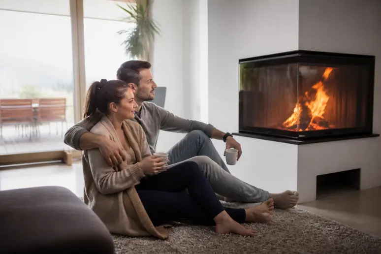 Un couple profite de la chaleur d'une cheminée d'angle moderne dans un salon lumineux, ambiance conviviale.