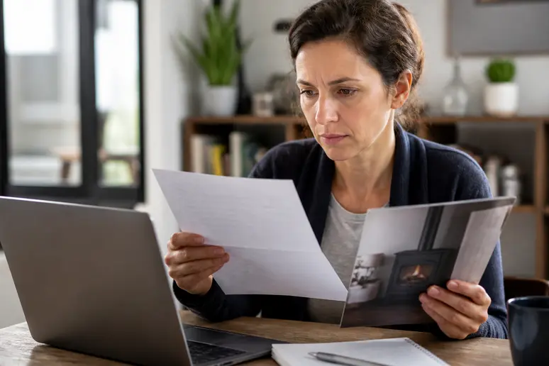 Femme française examinant attentivement des documents, s'informant sur les aides financières pour l'achat d'un poêle performant.