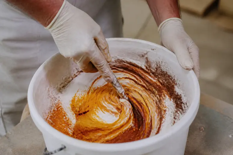 Mains gantées mélangeant des pigments naturels dans de l'enduit à la chaux pour une personnalisation de couleur.