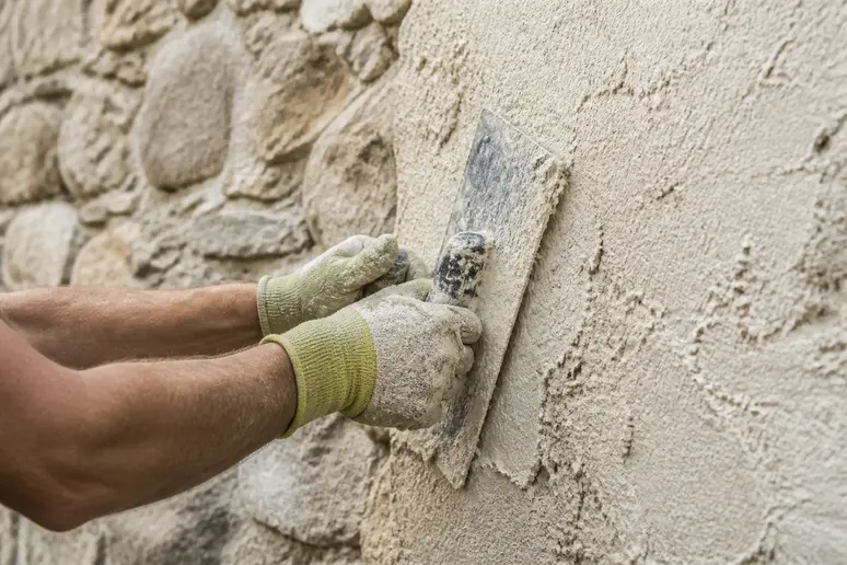 Mains d'un artisan appliquant avec soin un enduit à la chaux sur un mur de pierre ancien.
