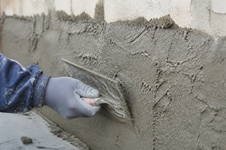 Application soignée d'enduit de soubassement à la truelle sur le bas d'un mur extérieur, garantissant une couche uniforme.