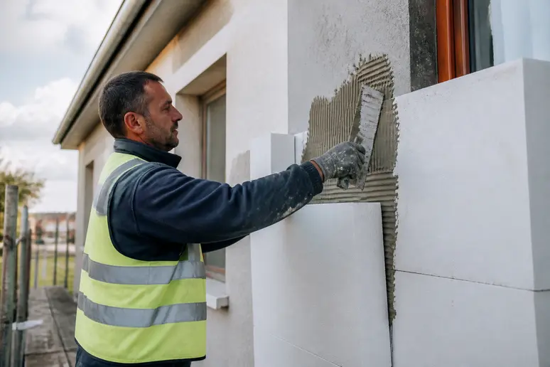 Un ouvrier applique des panneaux isolants sur une façade extérieure, assurant une pose méticuleuse et professionnelle du matériau.