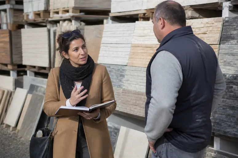 Une femme consulte un employé pour comprendre le budget nécessaire pour un mur extérieur en pierre naturelle.