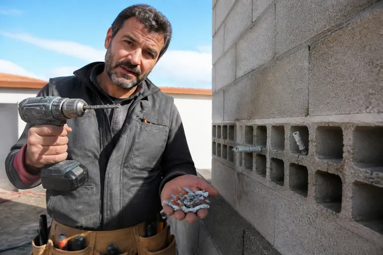 Un artisan français montre différentes chevilles pour fixer un bardage sur un mur en parpaing creux.
