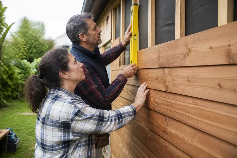 Un couple français supervise les étapes clés de la pose d'un bardage bois sur leur maison.
