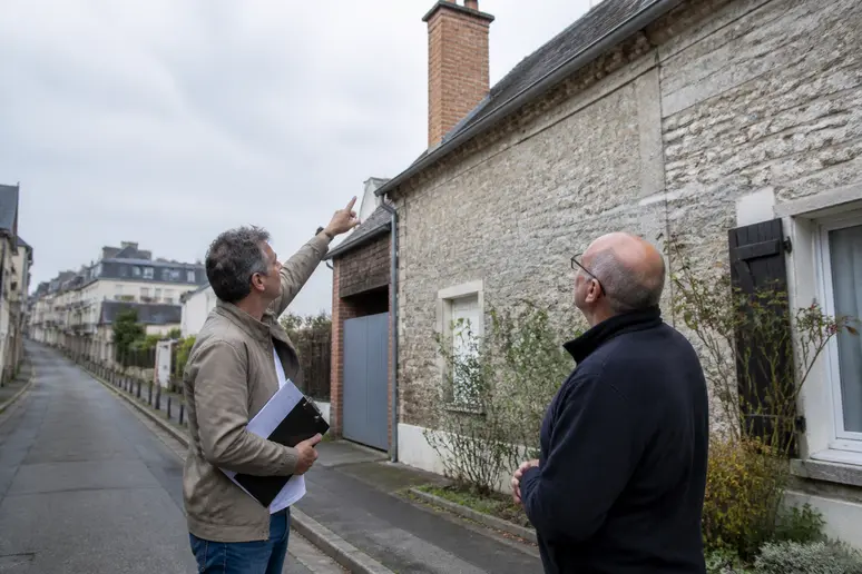 Un homme montre une cheminée à un propriétaire, illustrant l'obligation de ramonage à Rouen pour la sécurité de l'habitat.