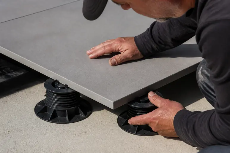 Pose d'une dalle grise de terrasse sur plots réglables en plastique pour une structure surélevée