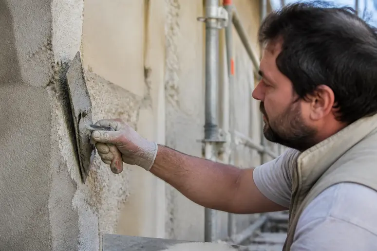 artisan façadier appliquant un enduit extérieur avec une truelle sur un mur à rénover