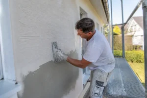 Artisan réalisant un enduit sur un mur avec une entreprise crepi exterieur pour la rénovation d'une maison