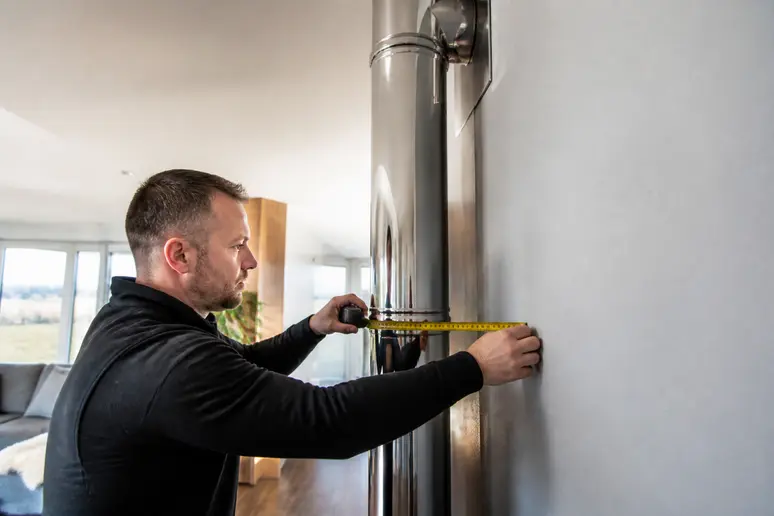 Technicien mesurant la distance de sécurité d'un conduit de poêle à bois selon les normes