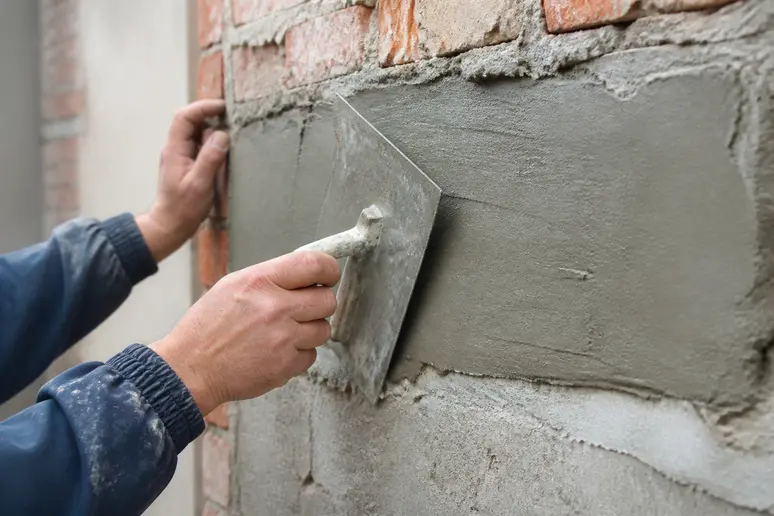 Application à la truelle d'un enduit de façade pour la rénovation d'un muret extérieur.