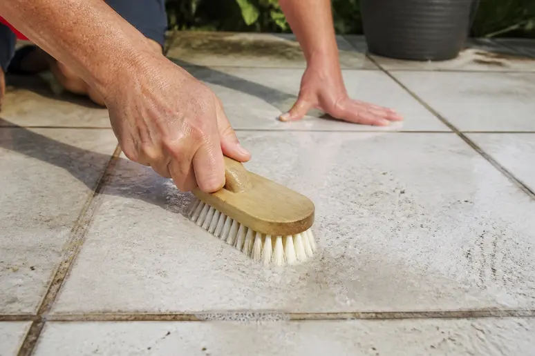 Nettoyage manuel d'un carrelage de terrasse blanche avec une brosse souple et de l'eau.
