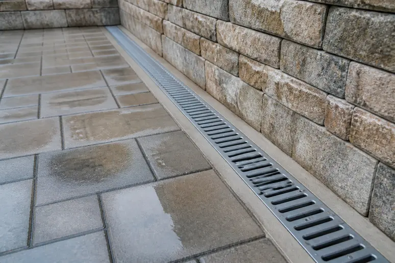 Caniveau à grille métallique installé au pied d'un mur de soutènement pour le drainage d'une terrasse encaissée