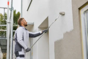 Un artisan applique un enduit sur un mur de maison pour savoir comment faire un crépi extérieur au rouleau.