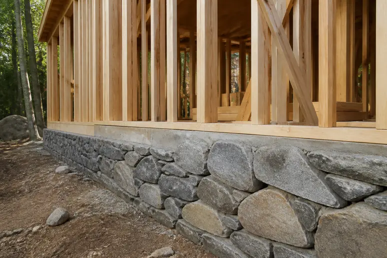 Jonction entre un soubassement en pierre naturelle et une ossature bois sur un chantier de construction