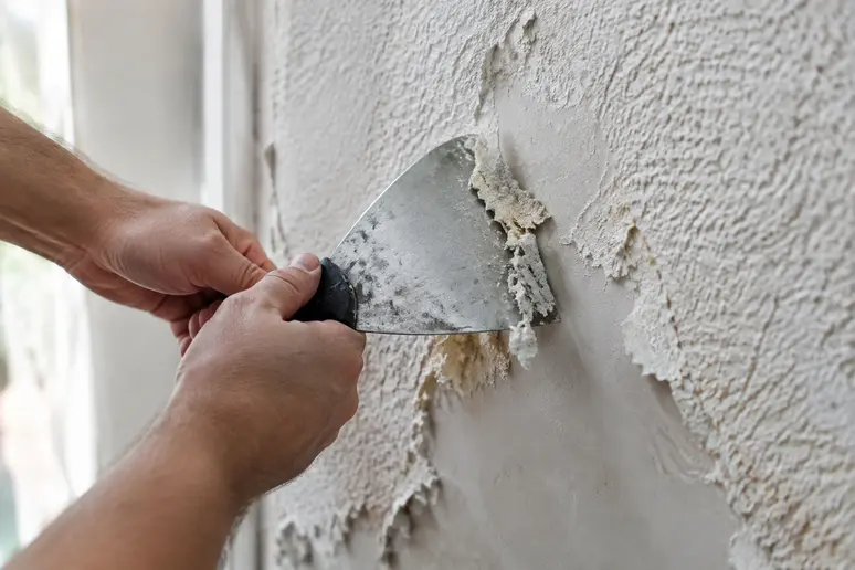 Utilisation d'une spatule pour gratter un crépi intérieur texturé lors de la rénovation