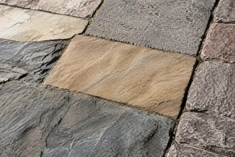 Échantillons de pavés rustiques en pierre naturelle, grès et béton disposés en extérieur.