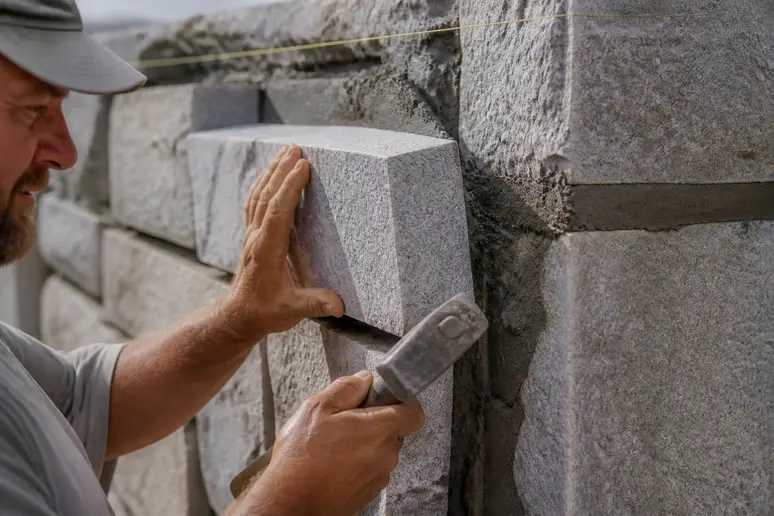 Maçon ajustant un bloc de pierre de taille en granit sur un mur de façade.