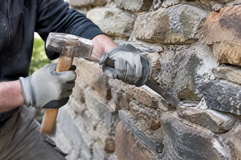 Artisan dégarnissant les joints d'un mur en pierre avec un burin plat