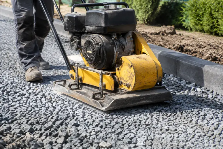 Compactage mécanique d'une couche de fondation en grave pour stabiliser l'allée.