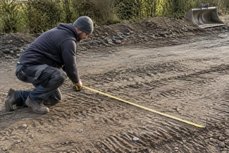 Un artisan mesure l'écart entre les bandes de roulement d'allée pour préparer le terrain.