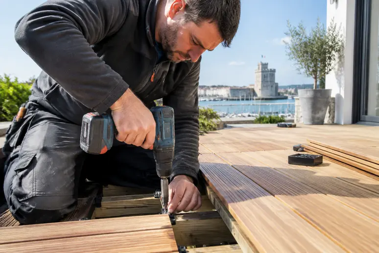 Artisan posant des lames de terrasse bois sur mesure avec fixation invisible à La Rochelle.